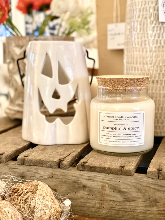 Natural Soy Wax Candle in a Clear Glass Apothecary-Style Jar and a Cork Lid. White Label on the Jar Reads "chester candle company. Fragrance No. 17. pumpkin & spice with hints of vanilla and brown sugar. 100% Natural Soy Wax, Cotton Wick, Natural Fragrance. 16 ounces 50-60 hours. Poured in Chester, NJ”