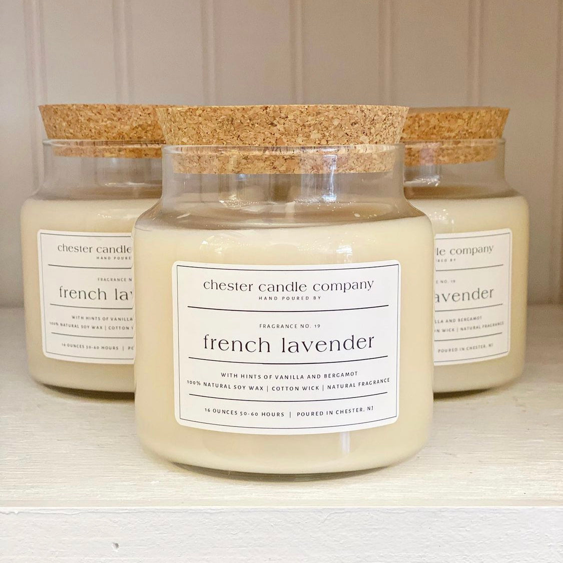 Natural Soy Wax Candle in a Clear Glass Apothecary-Style Jar and a Cork Lid. White Label on the Jar Reads "chester candle company. Fragrance No. 19. french lavender with hints of vanilla and bergamot. 100% Natural Soy Wax, Cotton Wick, Natural Fragrance. 16 ounces 50-60 hours. Poured in Chester, NJ”