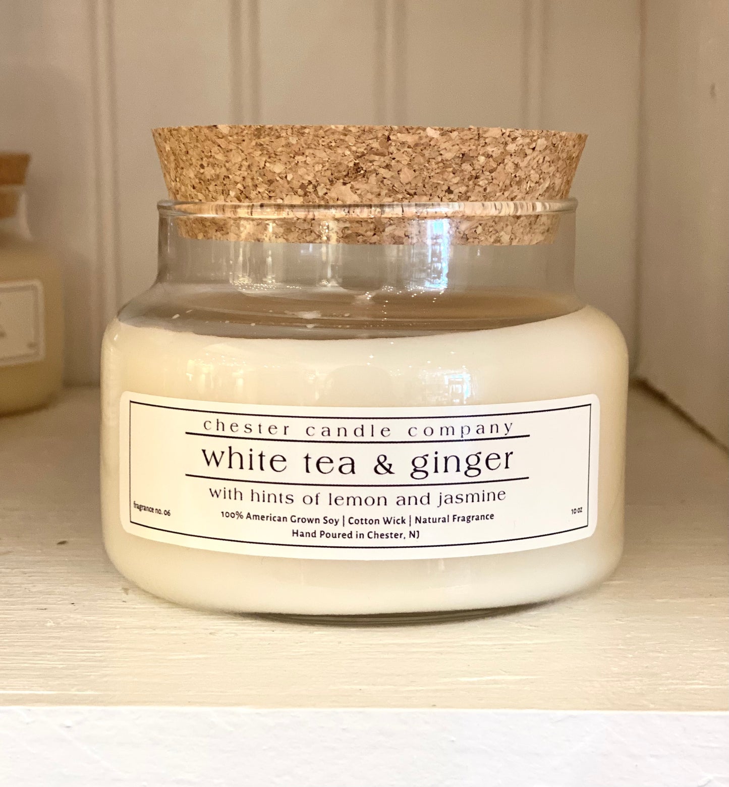 Natural Soy Wax Candle in a Clear Glass Apothecary-Style Jar and a Cork Lid. White Label on the Jar Reads "chester candle company. White tea & ginger with hints of lemon and jasmine. 100% American Grown Soy, Cotton Wick, Natural Fragrance. Fragrance No. 06 Hand Poured in Chester, NJ. 10oz”
